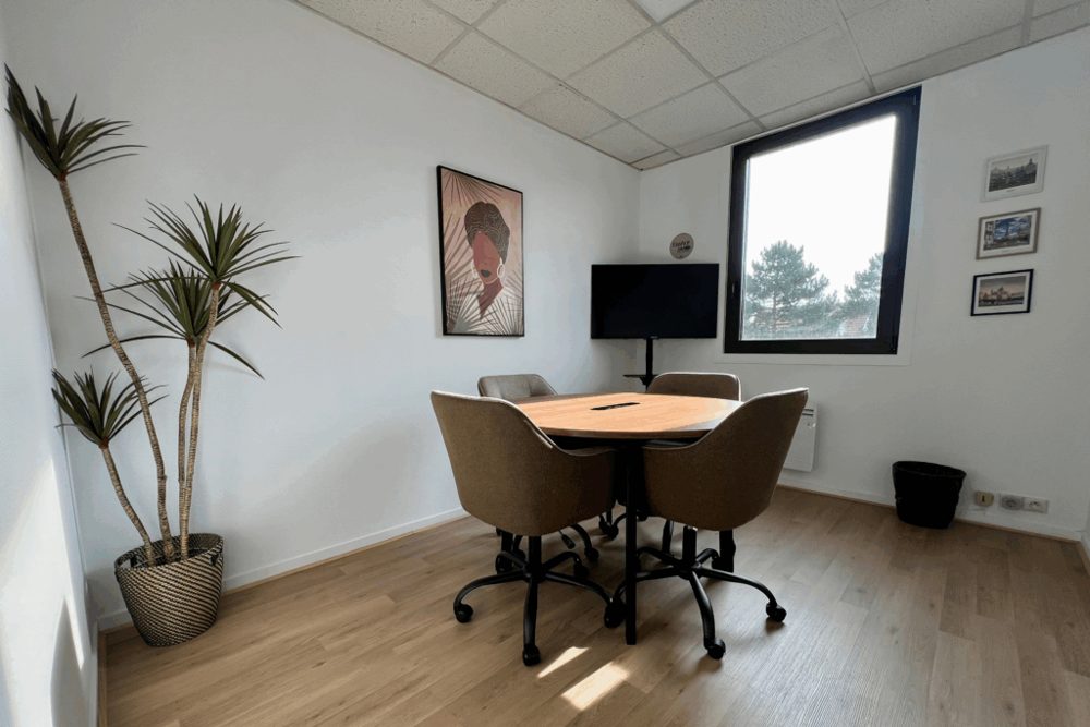 La salle de réunion : une table ronde, quatre fauteuils, un écran sur pied, une plante